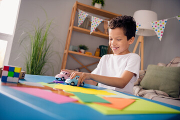 Photo of cheerful positive little boy dressed white t-shirt sitting table enjoying game indoors house home room