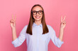 Photo of professional young girl makes peace gesture shows v sign isolated pink color background
