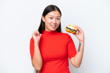 Wall Mural - Young Asian woman holding a burger isolated on white background proud and self-satisfied