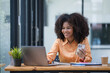 canvas print picture - Portrait of a beautiful confident businesswoman using a laptop computer holding a mobile phone sitting in a modern office. Smiling African American freelancer working online from home. 