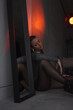 © NASTYA PALEHINA - teen girl in shiny bodysuit is sitting fashion in profile with closed eyes on floor near mirror with hand on knee on gray wall background in loft interior with red light. fashion concept, free space