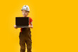 © somemeans - Serious schoolboy in work clothes and protective helmet holds laptop with empy screen. Copy space, mock up. Child as architect