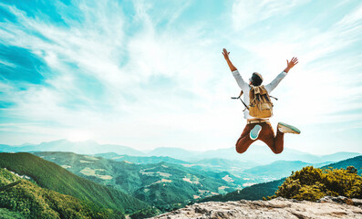 Wall Mural - Happy man with backpack jumping on top of the mountain - Delightful hiker with arms up standing over the cliff - Sport and travel life style concept