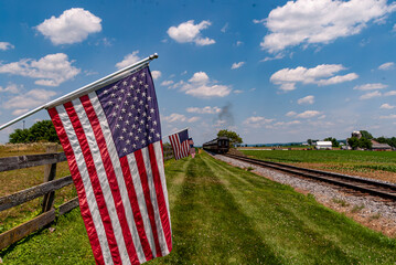 Canvas Print - View of American Flags Waving on a Fence After a Steam Passenger Train Passed on a Sunny Summer Day