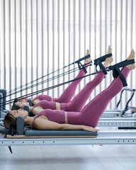 Wall Mural - Three Asian women in pink sportswear doing pilates exercises with a reformer bed. 