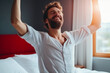 © MVProductions - Handsome happy man stretching on bed in the morning, wake up stretch, good mood in the morning. Generative AI