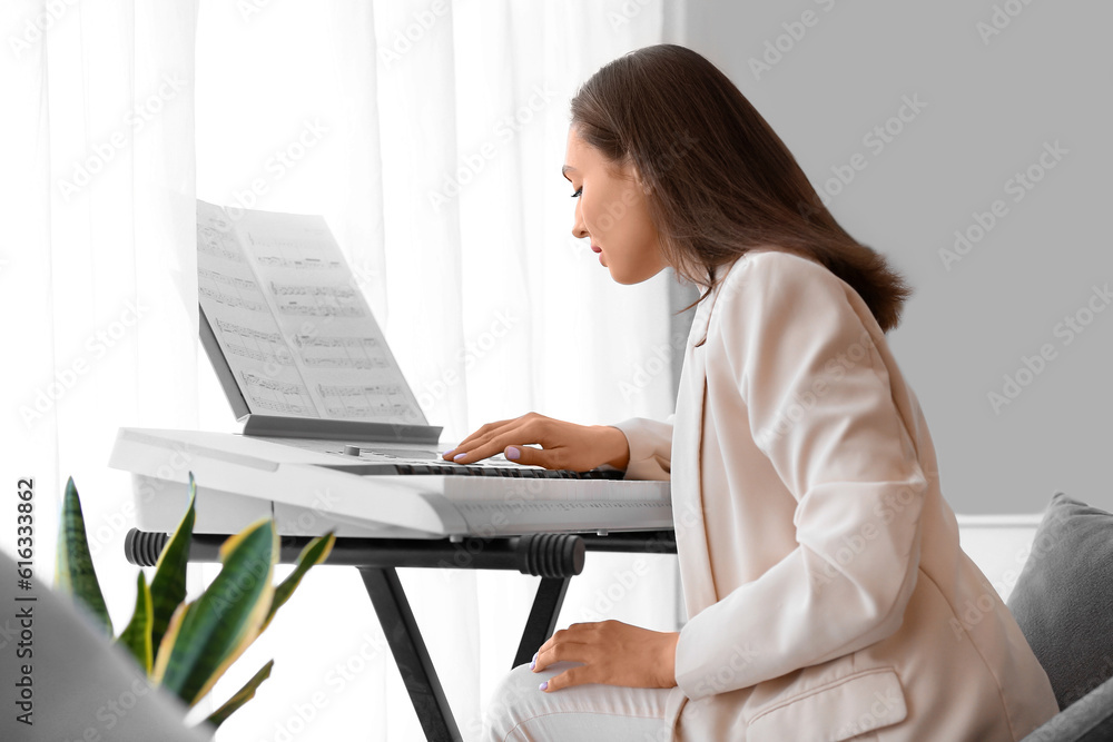 Young female musician playing synthesizer at home