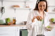 © Pixel-Shot - Young woman putting cucumber slices into blender in kitchen