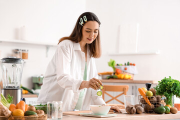 Young woman measuring cucumber slices on scales in kitchen