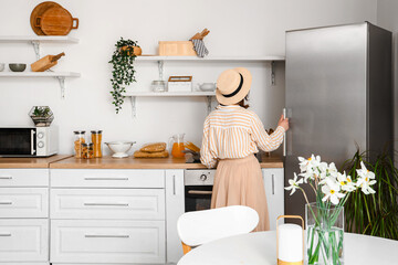 Wall Mural - Young woman opening stylish fridge in kitchen