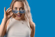 © Pixel-Shot - Young woman in stylish sunglasses on blue background, closeup