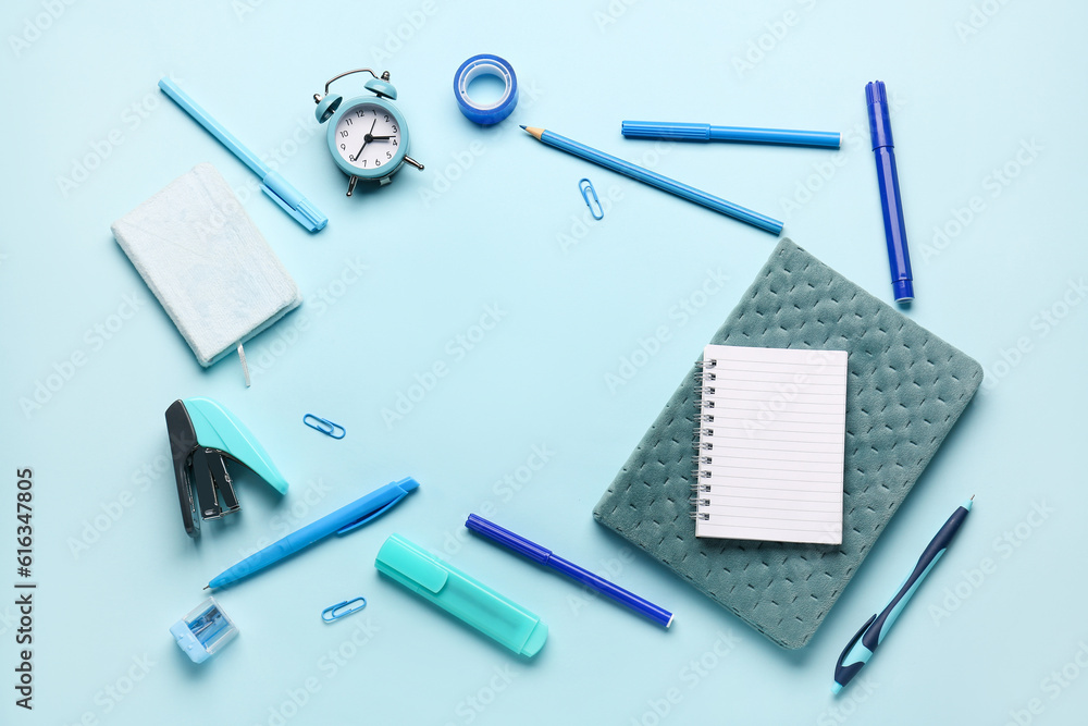Notebooks with alarm clock and frame made of different stationery on blue background