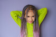 A pretty girl with purple braided pigtails made of artificial hair looks innocently at the camera