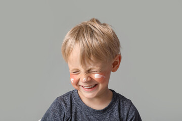 allergic little boy with sunburned face and cream on grey background, closeup