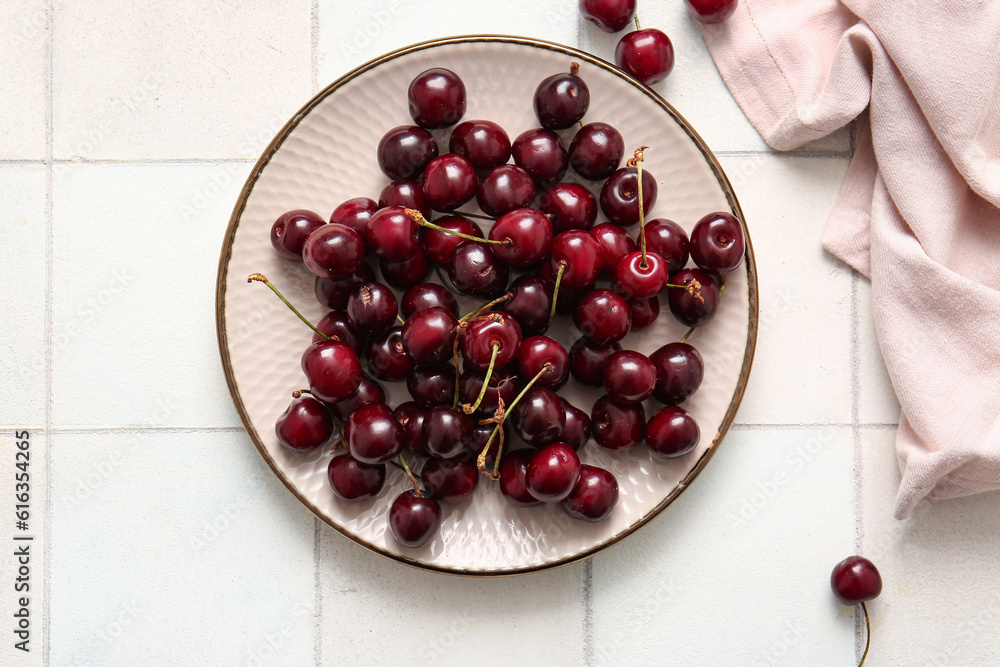 Plate with sweet cherries on white tile table