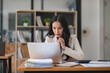 © chartchai - A thoughtful Asian businesswoman focuses on her tasks on her laptop, looking at her laptop with a serious face, and working at her desk in the office.