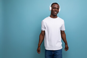 Wall Mural - young african man in white t-shirt listening to music with white headphones on studio background with copy space