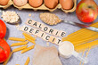 the inscription calorie deficit next to healthy food products. Flat lay photo showing weight loss and getting in shape