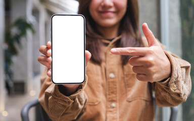 Mockup image of a young woman holding, showing and pointing finger at a mobile phone with blank white screen