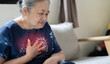 Senior Asian woman suffering from chest pain while sitting on the sofe at home.