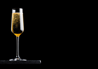 Elegant glass of yellow champagne with bubbles on black marble board on black background. Space for text