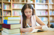 © FotoArtist - Smiling student girl in eyeglasses reading a red book in a library. School and education concept