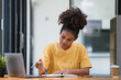 © Songsak C - A beautiful African American girl, student or businesswoman sitting at a desk and writing.