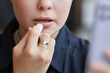 © Seventyfour - Minimal closeup of young woman doing makeup and using nude lipstick color looking in mirror, copy space