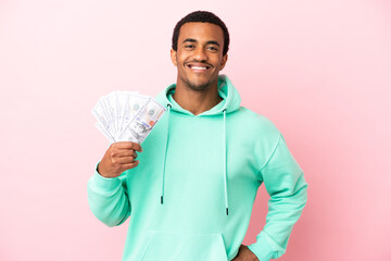 Wall Mural - Young man taking a lot of money over isolated pink background posing with arms at hip and smiling