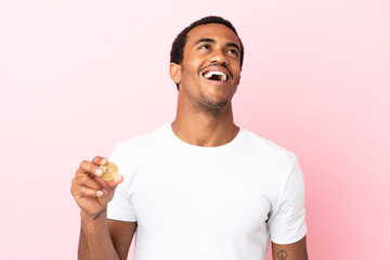 Wall Mural - Young African American man holding a Bitcoin over isolated pink background laughing