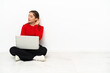 © luismolinero - Young caucasian woman with a laptop sitting on the floor listening to something by putting hand on the ear