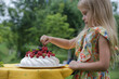 Adorable little girl in floral summer dress eating Pavlova cake
