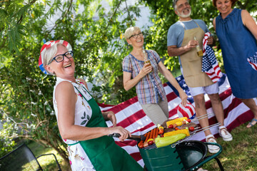 A group of elderly people celebrates the 4th of July in a backyard while making barbeque.