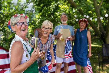 A group of elderly people celebrates the 4th of July in a backyard while making barbeque.