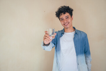 Young curly man with denim clothes hold a glass water. Smile, cheers and happy expression. The photo is suitable to use for mineral water bottle promotion and healthy life advertising.