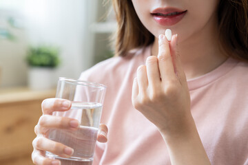 Sick, asian young woman, girl hand holding pill capsule, painkiller medicine from stomach pain, head ache, pain for treatment, take drug or vitamin and glass of water at home, pharmacy and health care