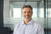 Happy Mid Aged Older Business Man Executive Standing In Office. Smiling 50 Year Old Mature Confident Professional Manager, Confident Businessman Investor Looking At Camera, Headshot Close Up Portrait.