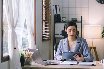 A portrait of a smiling, young, beautiful, professional, and confident millennial Asian businesswoman using a digital tablet to analyze sales data at a modern office.