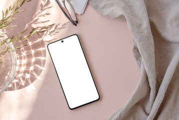 Blank smartphone screen mock up, linen textile, glass vase with meadow grass stems on neutral light pastel pink background with sunlight shadow. Aesthetic feminine business brand identity template