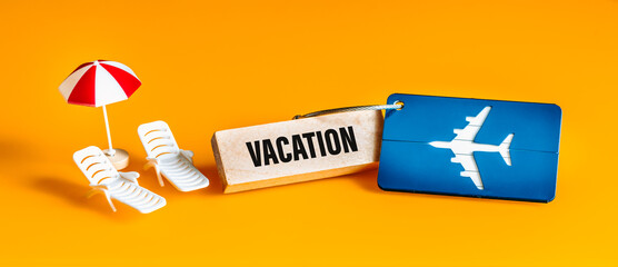 Fototapete - Vacation concept, Plane luggage tag, Sun loungers and umbrella miniature, Beautiful yellow background, Panorama, Written vacation on a wooden block