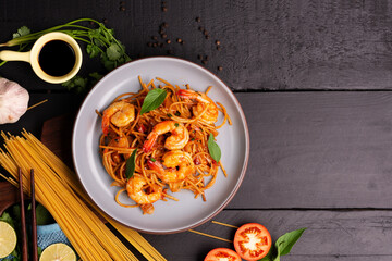 Wall Mural - Fried Spaghetti or Fried Noodles Tomato sauce and prawns on a blue plate On a black wooden table top, top view