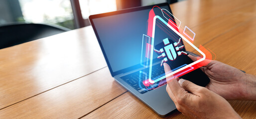 Businessman hands with phone and computer, a glowing bug virus on the screen