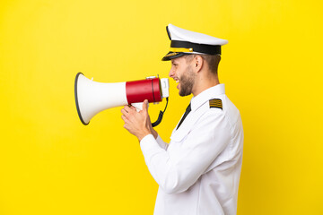 Wall Mural - Airplane caucasian pilot isolated on yellow background shouting through a megaphone