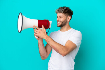 Wall Mural - Young handsome caucasian man isolated on blue background shouting through a megaphone to announce something