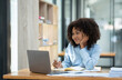 © crizzystudio - Positive successful african american woman, manager, CEO, sitting in the office at a laptop talking  video call with client or employee discussing business strategy and ideas analyzed together