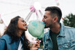 Young guys are having fun in an amusement park. Girlfriend and her boyfriend biting cotton candy during the festival.