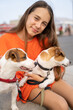 Beautiful teenage girl looking at camera hugging petting two dogs Jack Russell terriers lying on her laps. Friends portrait. Bright orange color t-shirt clothes