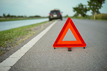 Wall Mural -  Red emergency stop sign with broken down car on the road waiting to be repaired. Close-up of red emergency stop sign placed on the road for vehicle accidents or breakdowns for road safety.