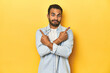 © Asier - Casual young Latino man against a vibrant yellow studio background, points sideways, is trying to choose between two options.