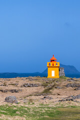 Wall Mural - A orange red lighthouse at the coast of iceland in summer on a really sunny day